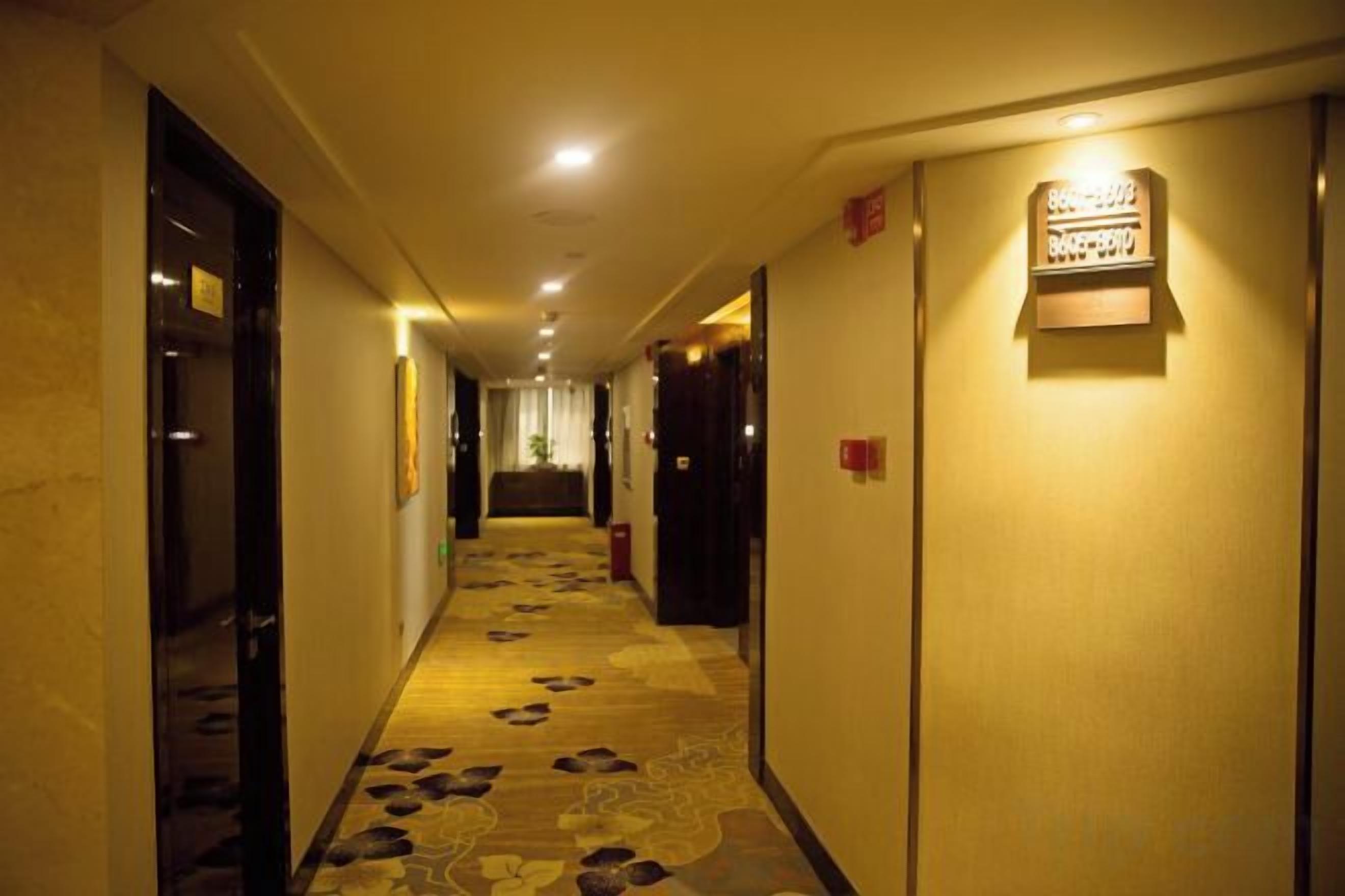 A hotel hallway with carpeted flooring, doors, and a wall-mounted light fixture.