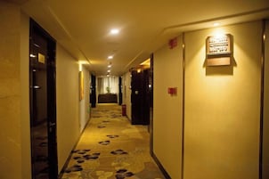 Un pasillo de hotel con piso alfombrado, puertas y una lámpara fijada a la pared.
