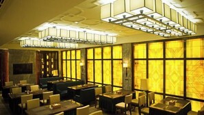 En restaurant med flere spiseborde og stole, et barområde og store vinduer med mønstret glas.