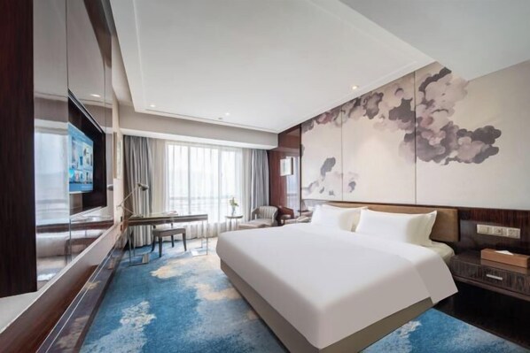 Ein Hotelzimmer mit einem großen Bett, einem Fernseher, einem Schreibtisch und einem Fenster mit Vorhängen.