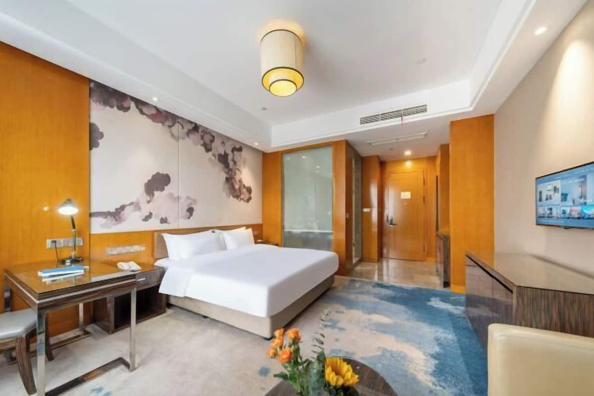 Een hotelkamer met een bed, bureau, stoel en een groot schilderij aan de muur.