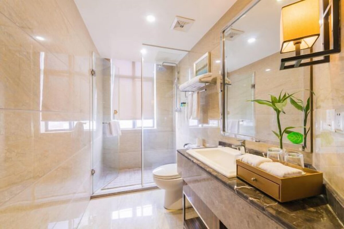 A modern bathroom with a glass shower enclosure, a large mirror, and a marble countertop.