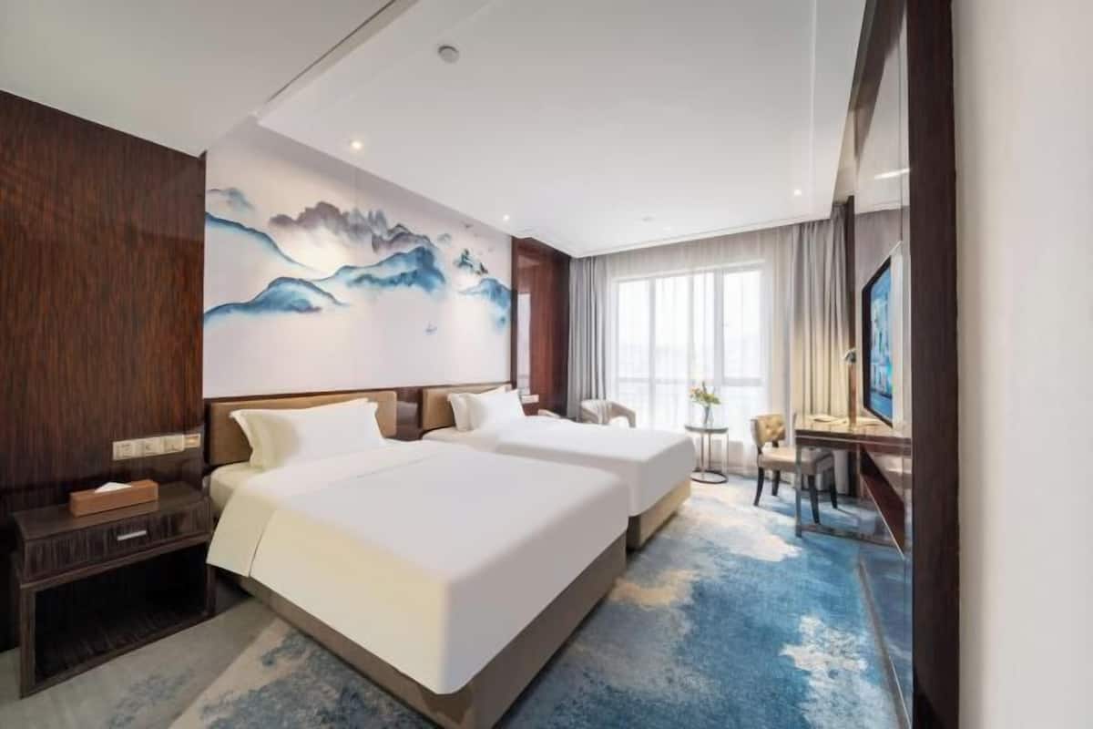 Een hotelkamer met twee bedden, een bureau, een stoel, een televisie en een schilderij aan de muur.