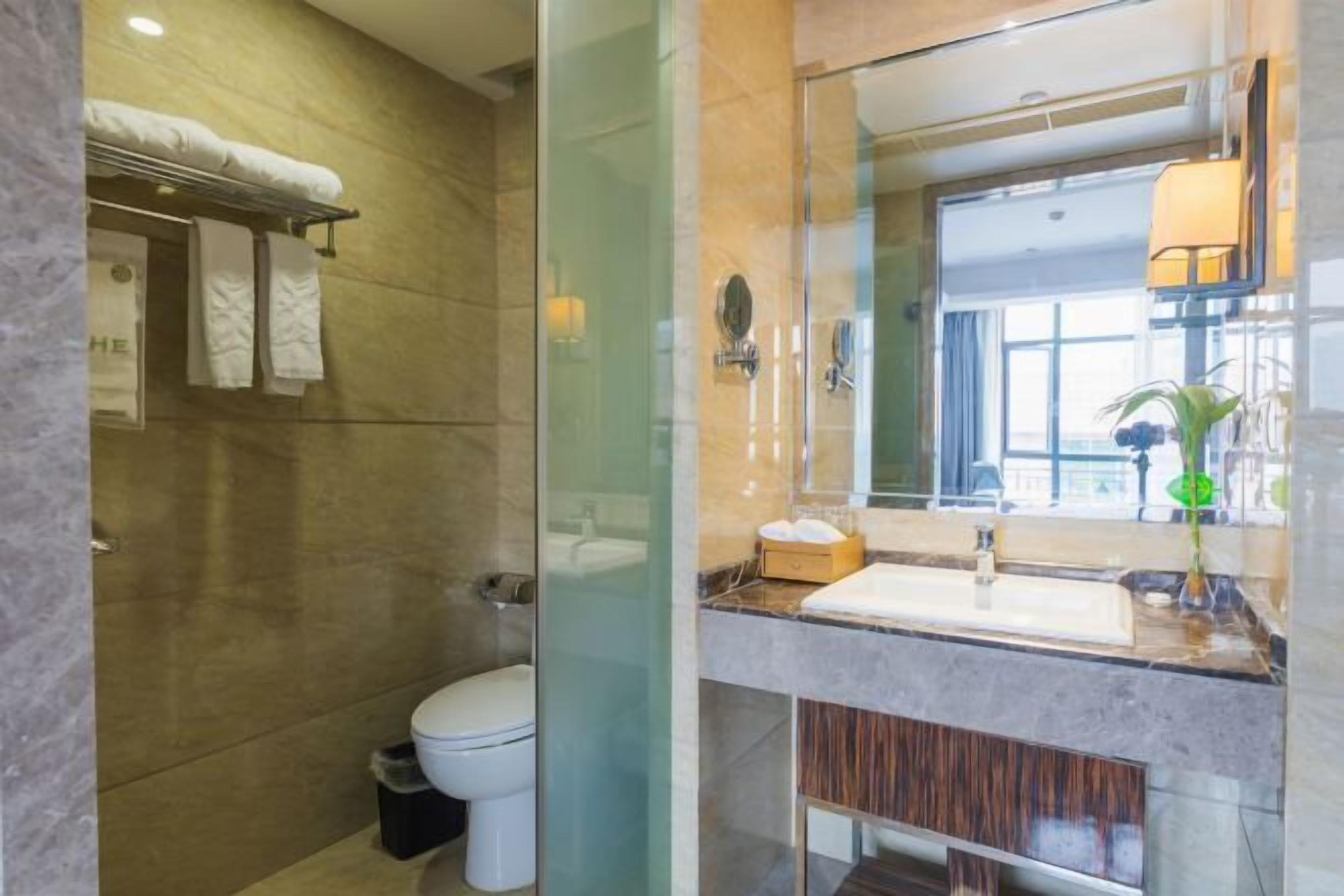 Un baño moderno con cabina de ducha de vidrio, inodoro blanco, tocador con espejo y perchero.