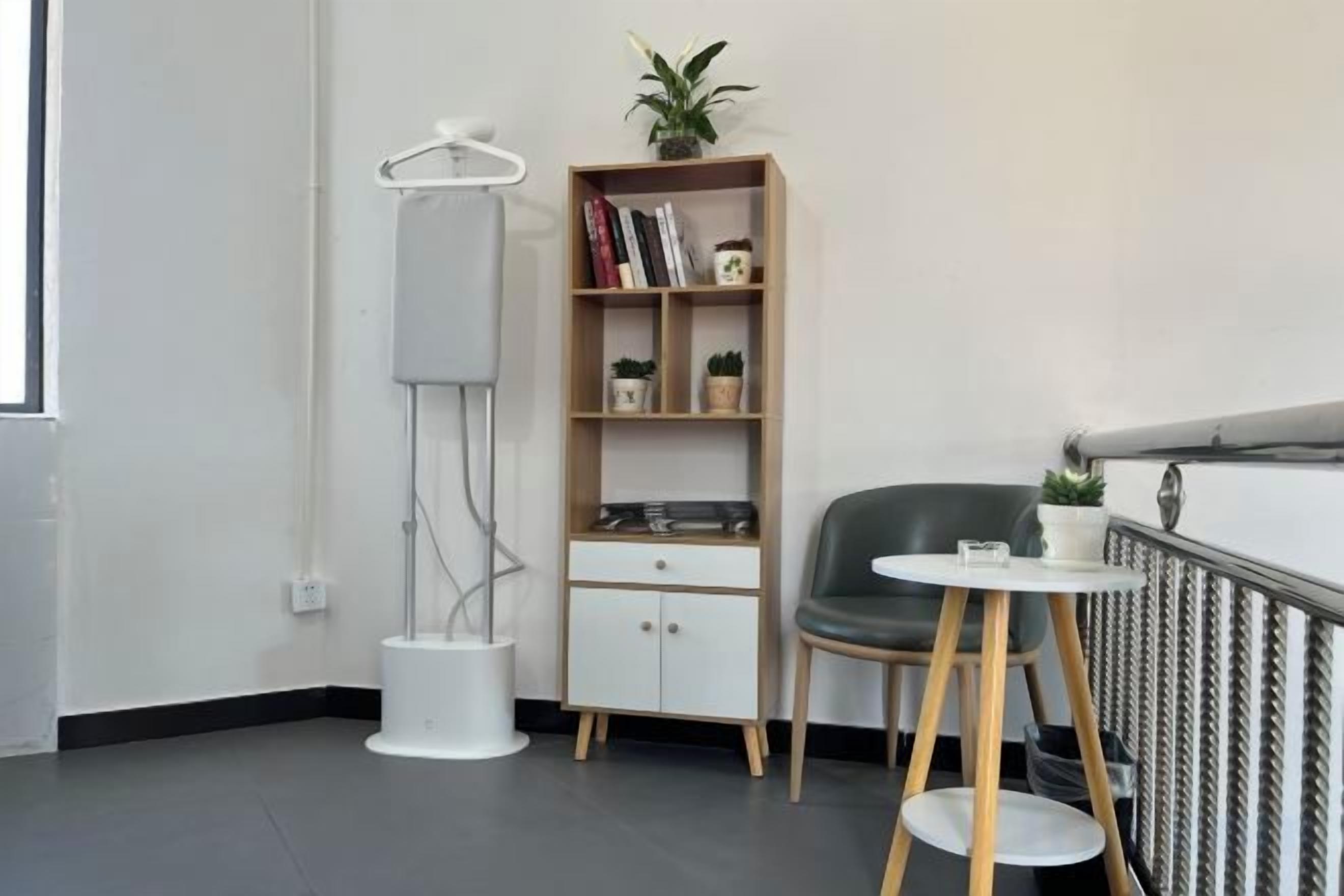 Una habitación con una silla moderna, una mesita, una estantería y una lámpara de pie.
