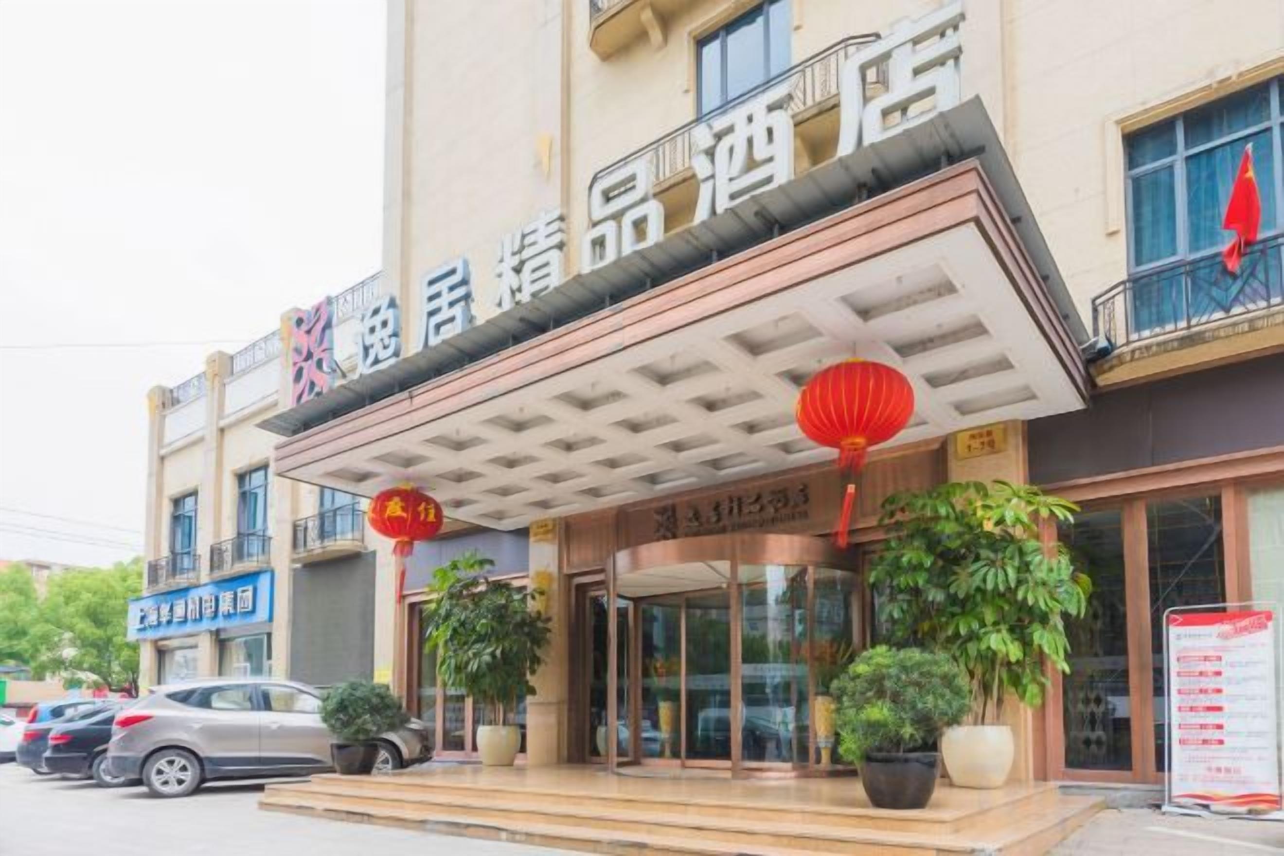 A hotel entrance with a covered walkway, potted plants, and a signboard.