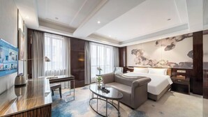 Et moderne hotelværelse med seng, sofa, skrivebord og et stort billede på væggen.