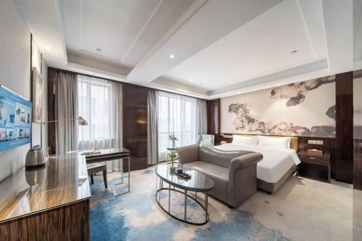 Een moderne hotelkamer met een bed, een bank, een bureau en een groot kunstwerk aan de muur.