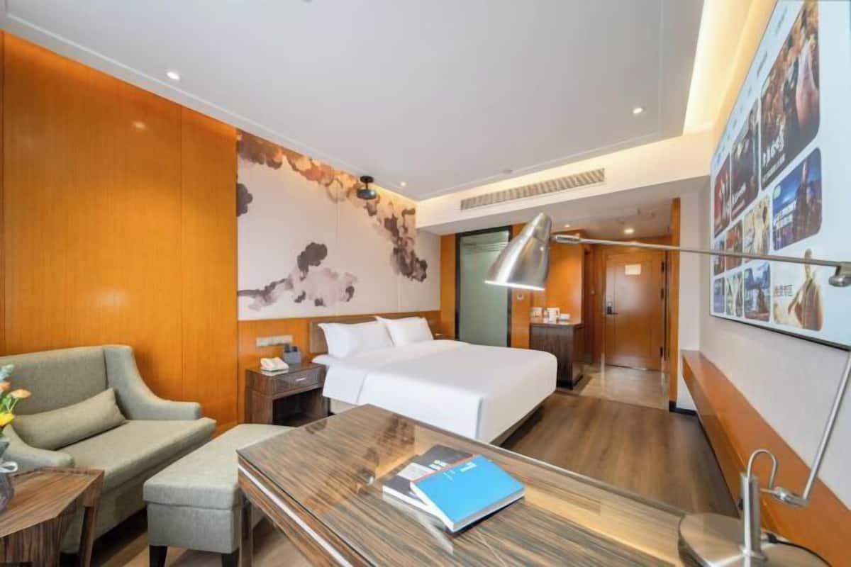 Een hotelkamer met een bed, een bureau, een stoel, een bank en een muur met een groot abstract kunstwerk.