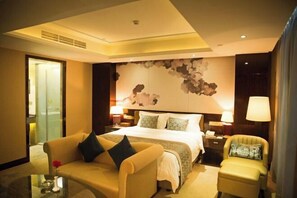 A hotel room with a large bed, a sofa, a chair, and a desk with lamps.