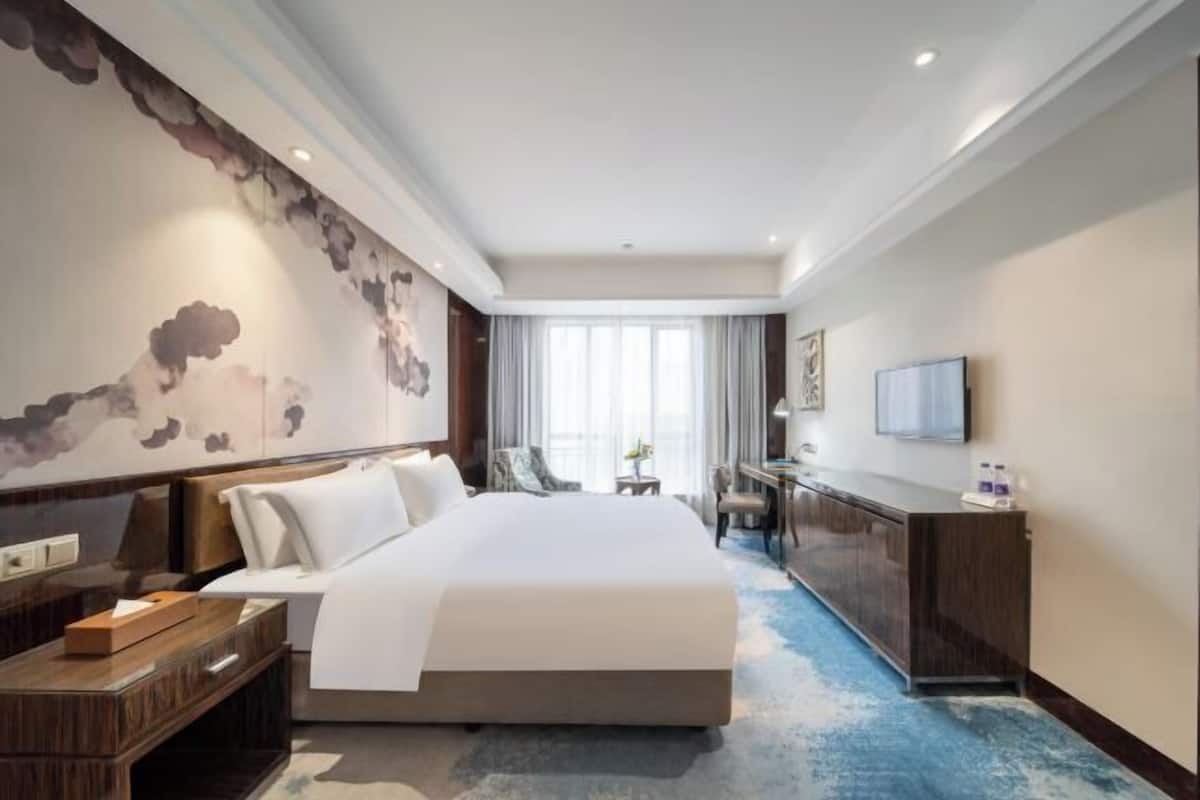 Een hotelkamer met een groot bed, een bureau, een stoel, een televisie en een raam met gordijnen.