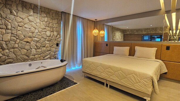 Een moderne slaapkamer met een stenen muur, een groot bed, een badkuip en een spiegel.