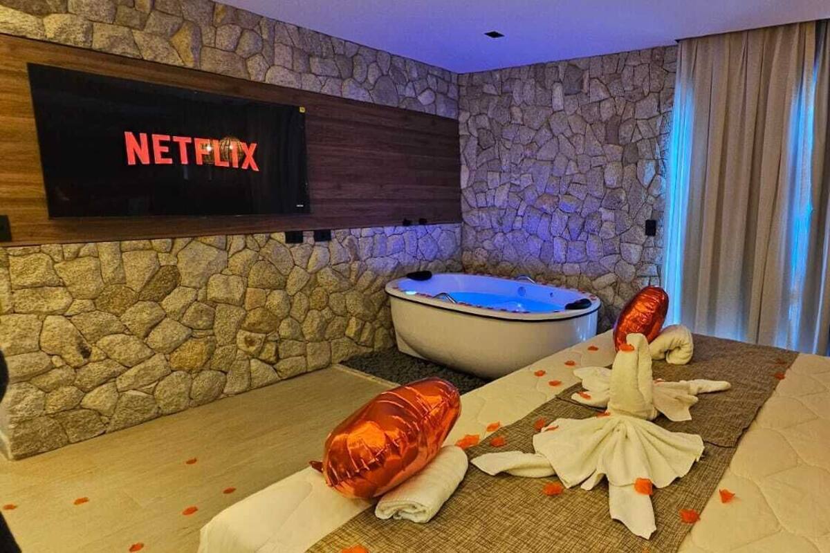 A room with a stone wall, a Netflix sign, a hot tub, and a massage table with towels and rose petals.