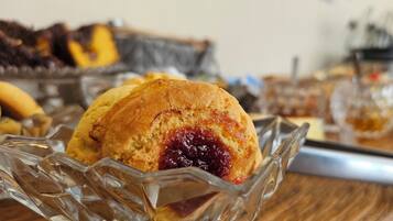 Een glazen schaal met gebak, waaronder een muffin met jam, op een houten tafel.
