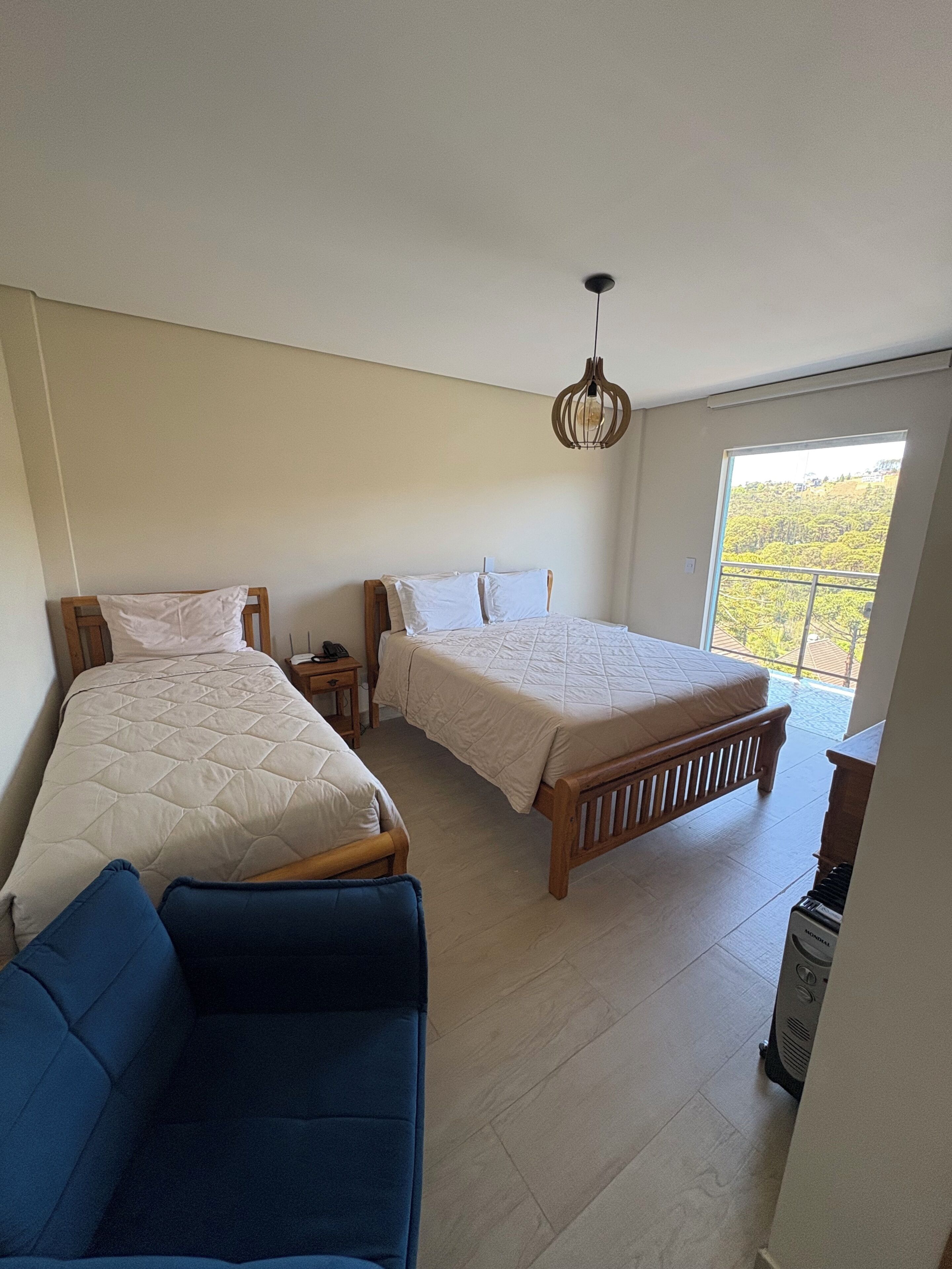 A bedroom with two beds, a blue sofa, a wooden bench, a nightstand, and a ceiling light fixture.
