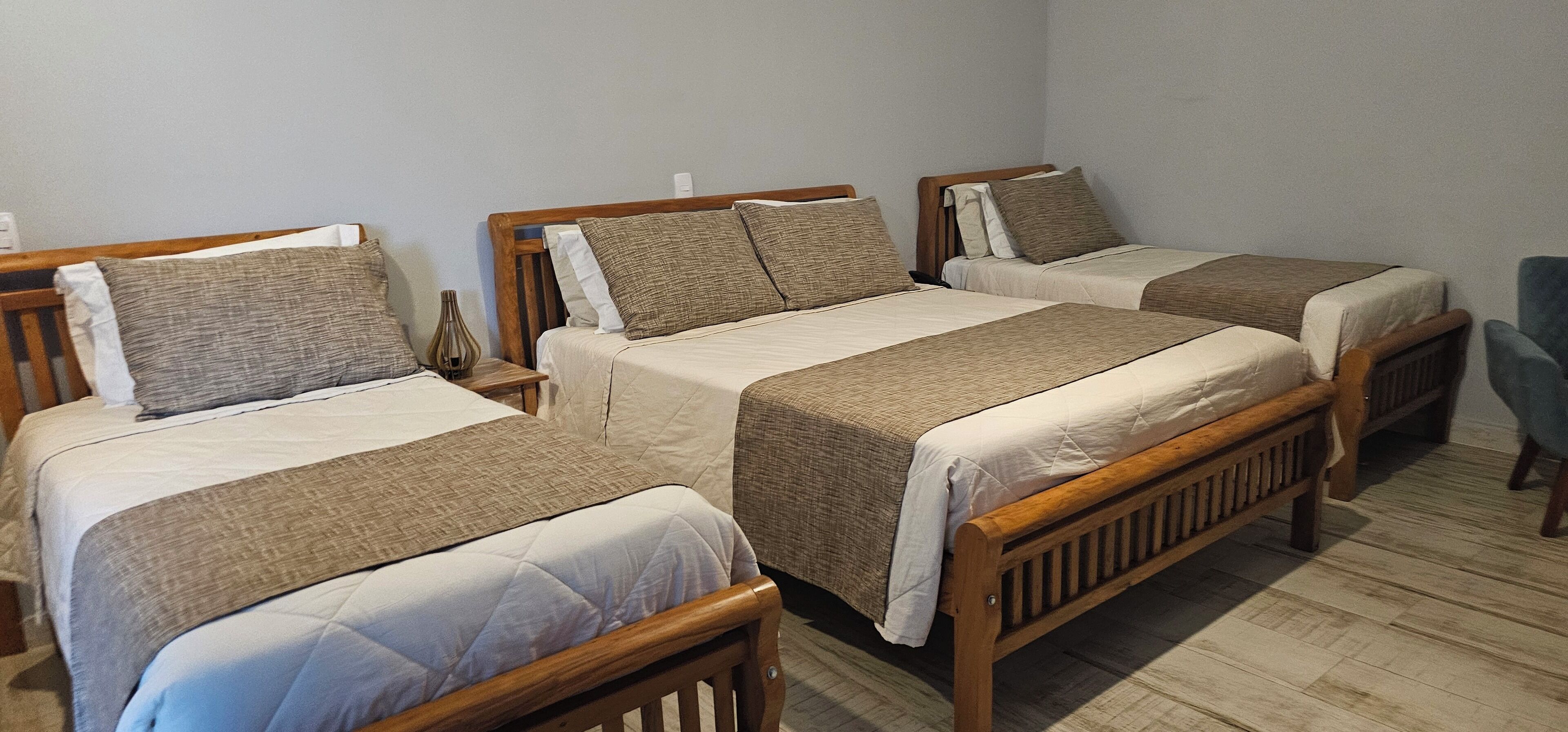 A room with three wooden beds, each with a quilted bedspread and pillows.