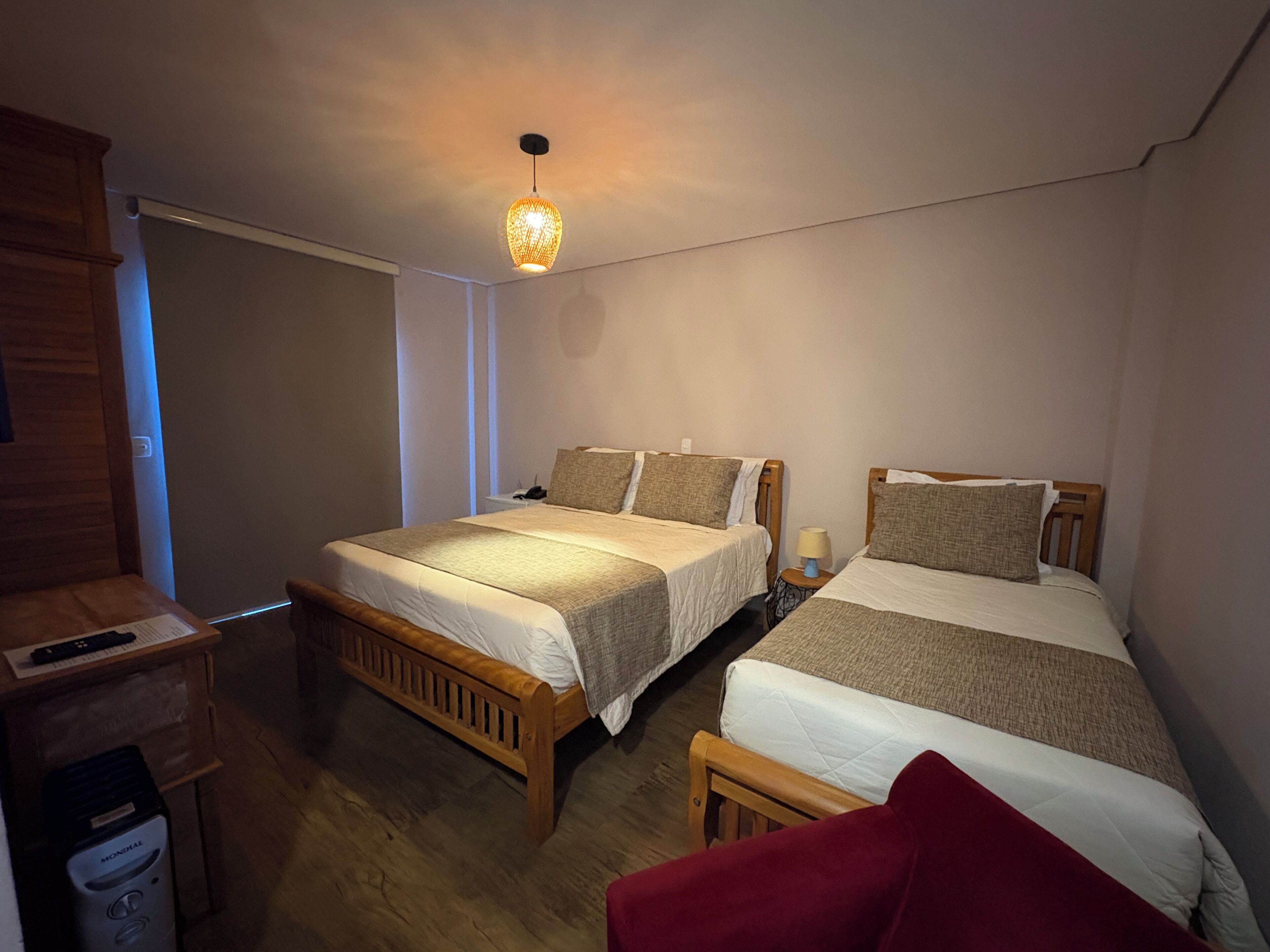 A bedroom with two single beds, a wooden wardrobe, a heater, and a hanging light fixture.