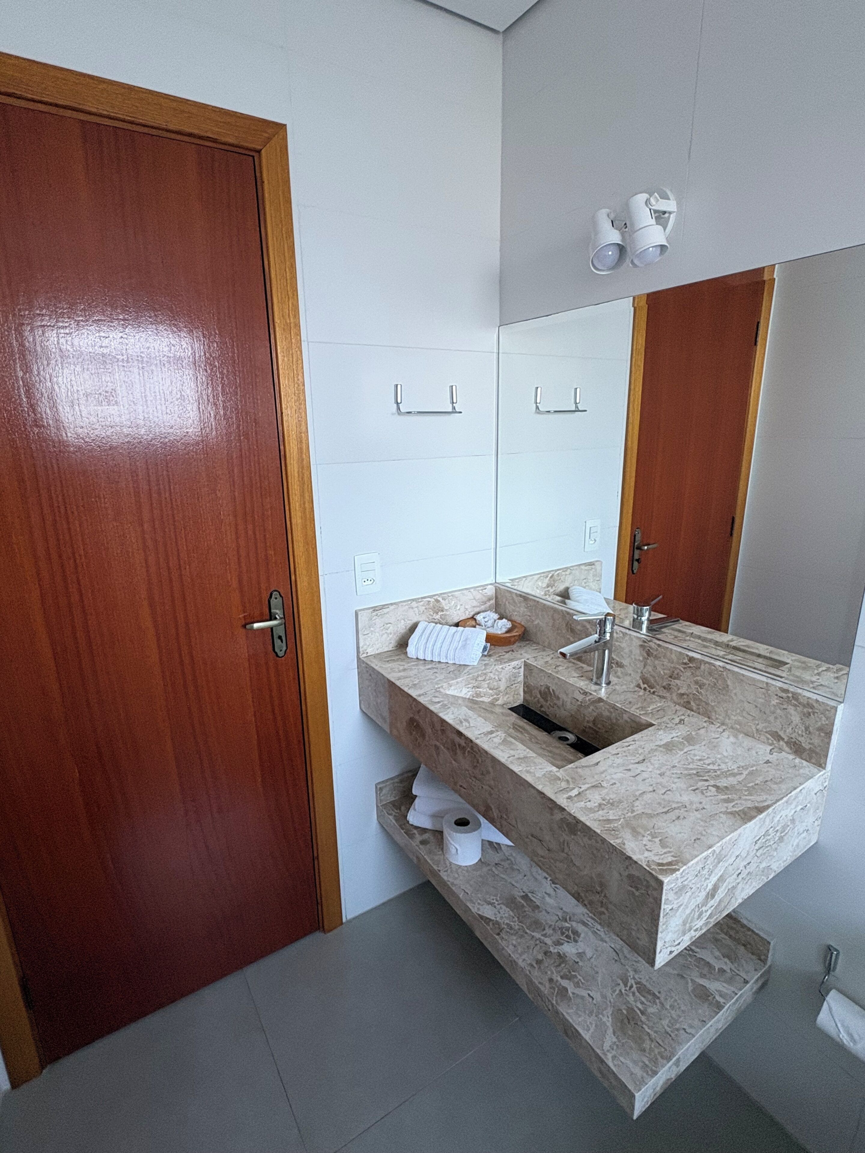A bathroom with a wooden door, a marble sink, a mirror, and a towel rack.