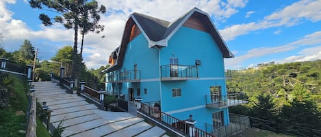 A multi-story building with a blue exterior, a wooden sloped roof, and balconies.