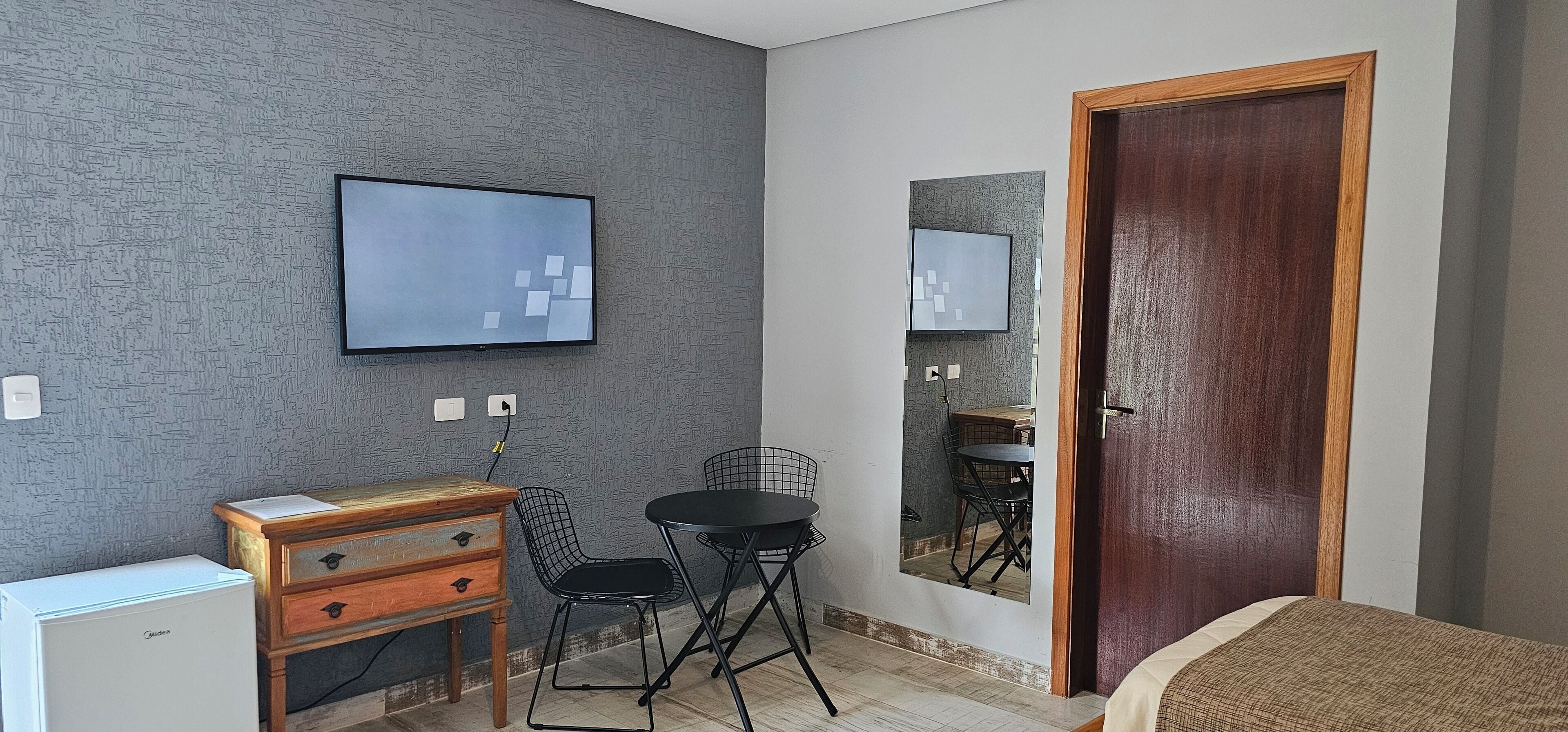 A small room with a bed, a desk with a chair, a television, and a door.