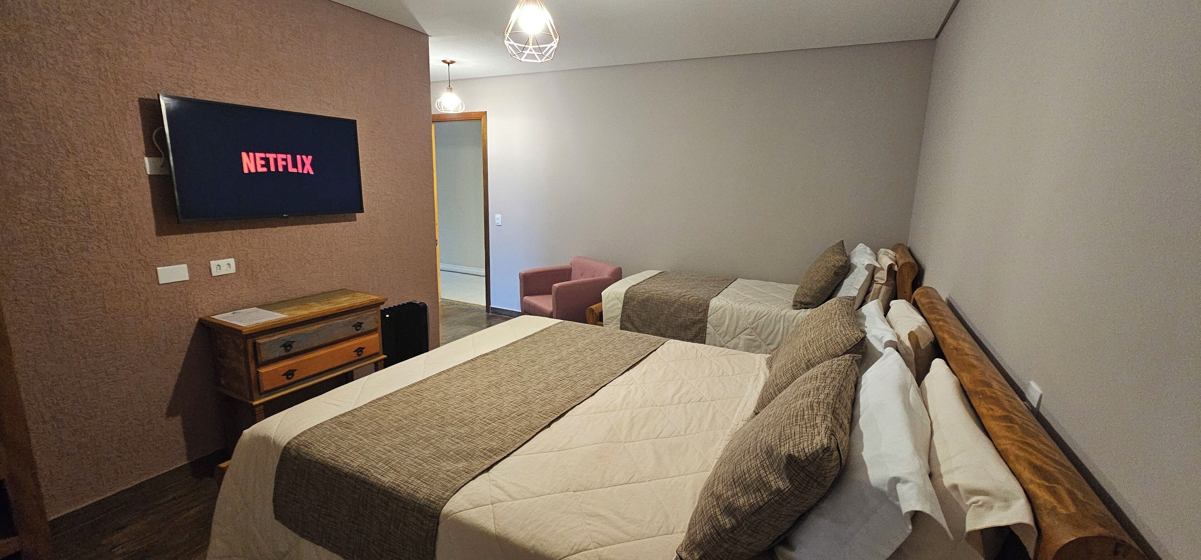 Une chambre d’hôtel avec deux lits, un téléviseur fixé au mur, une commode en bois et un miroir.