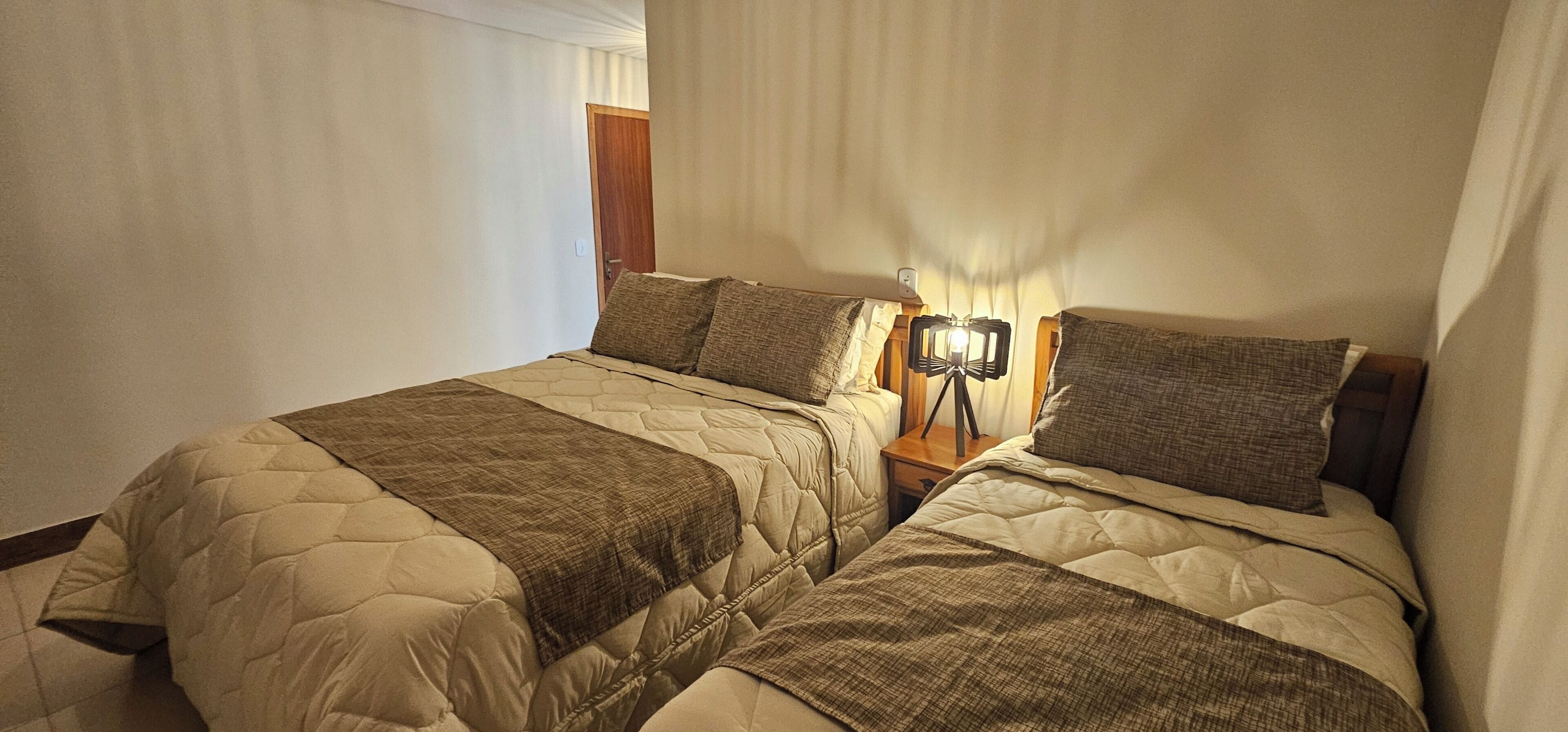A double bed with a quilted headboard and footboard, a bedside table with a lamp, and a wooden door in the background.