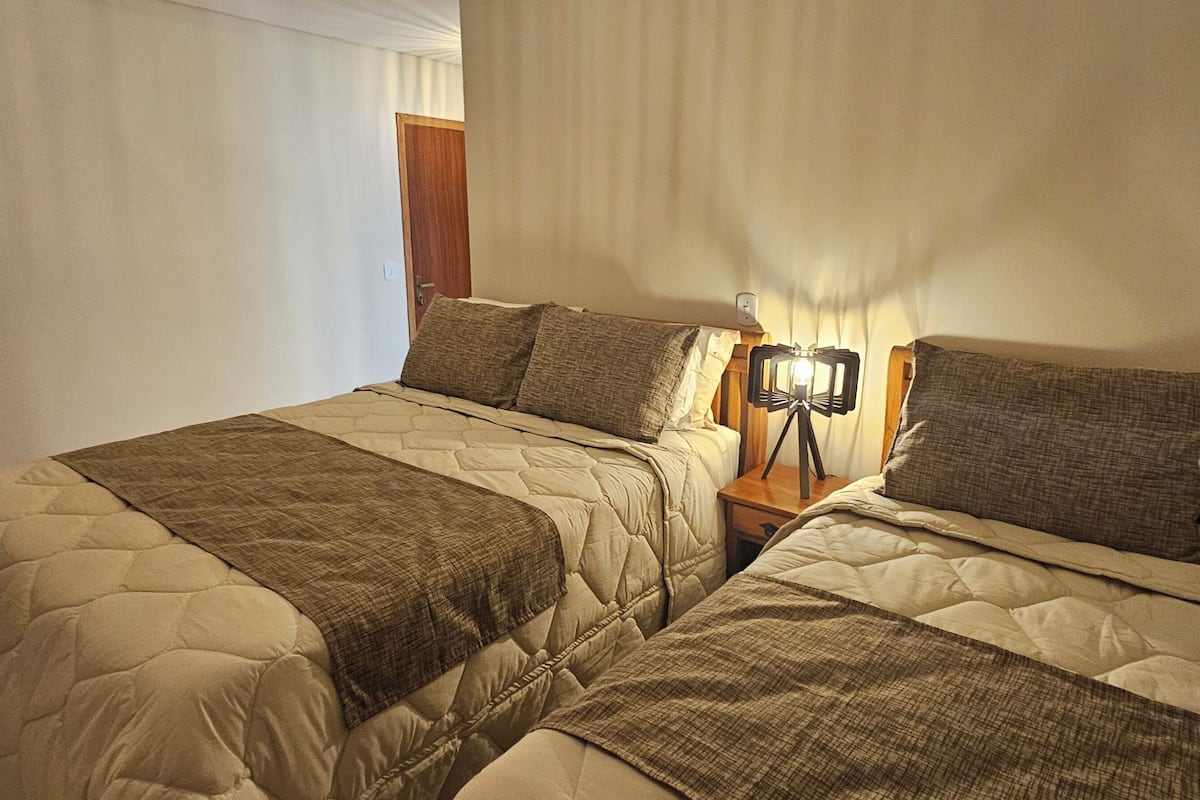 A double bed with a quilted headboard and footboard, a bedside table with a lamp, and a wooden door in the background.