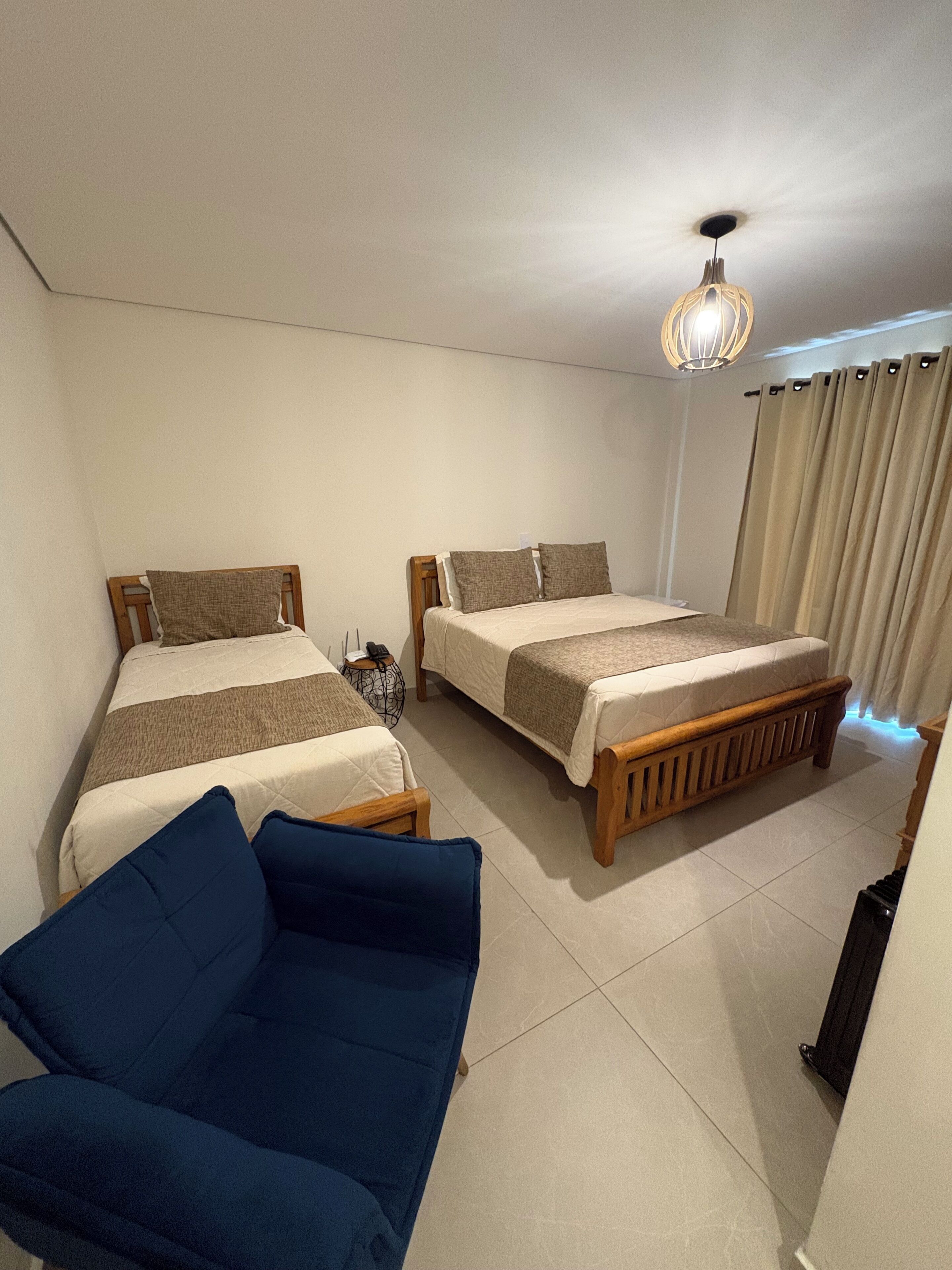 A hotel room with two beds, a blue sofa, a ceiling fan, and a window with curtains.