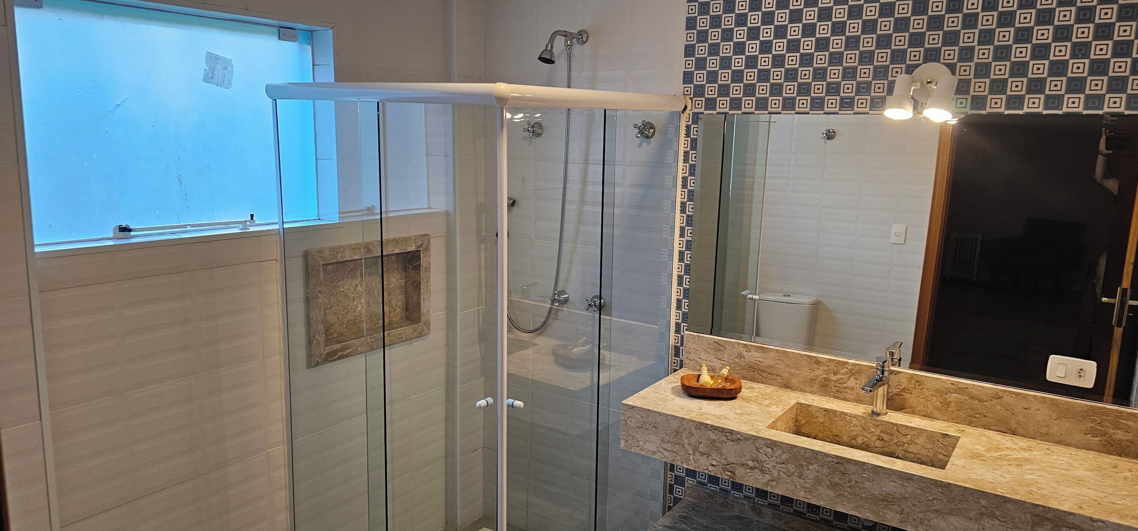A modern bathroom with a glass shower enclosure, a marble sink, and a patterned wall.