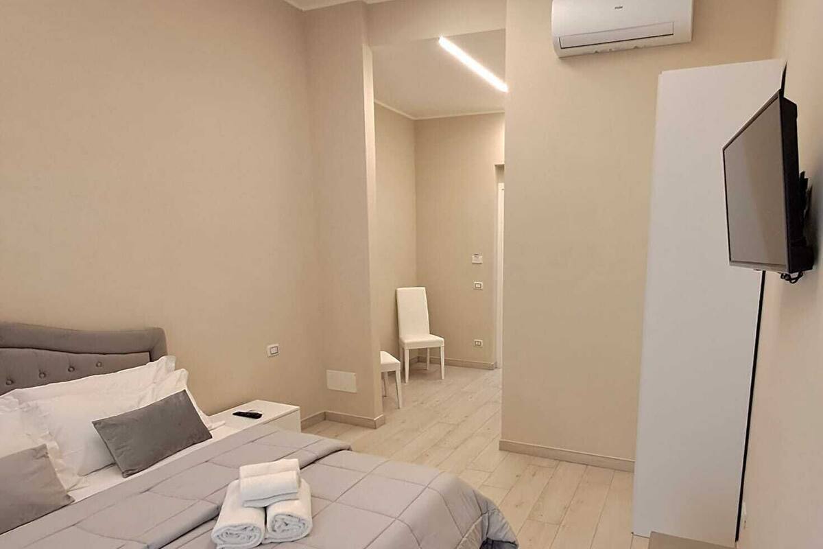 Quarto com cama, mesa de cabeceira, cadeira, televisão e aparelho de ar condicionado.