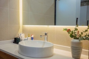 A bathroom with a round white sink, a mirror above it, and a vase with red flowers on the counter. - The Valley of Flowers (Lijiang)