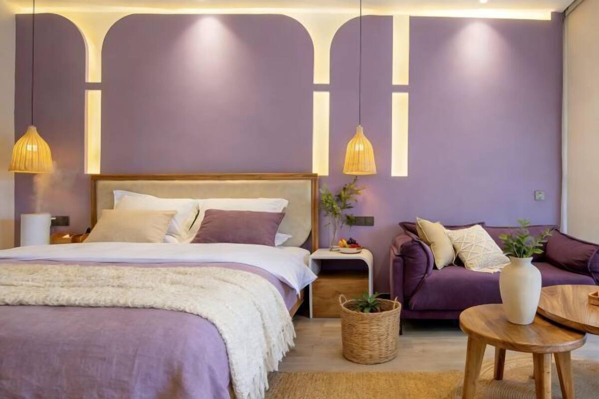 A bedroom with a bed, nightstand, and a purple sofa.