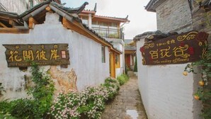 A narrow stone pathway flanked by traditional buildings with signage indicating a flower inn and a valley flowers establishment. - The Valley of Flowers (Lijiang)