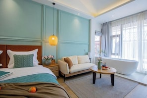 A hotel room with a bed, a sofa, a round coffee table, and a bathtub. - The Valley of Flowers (Lijiang)