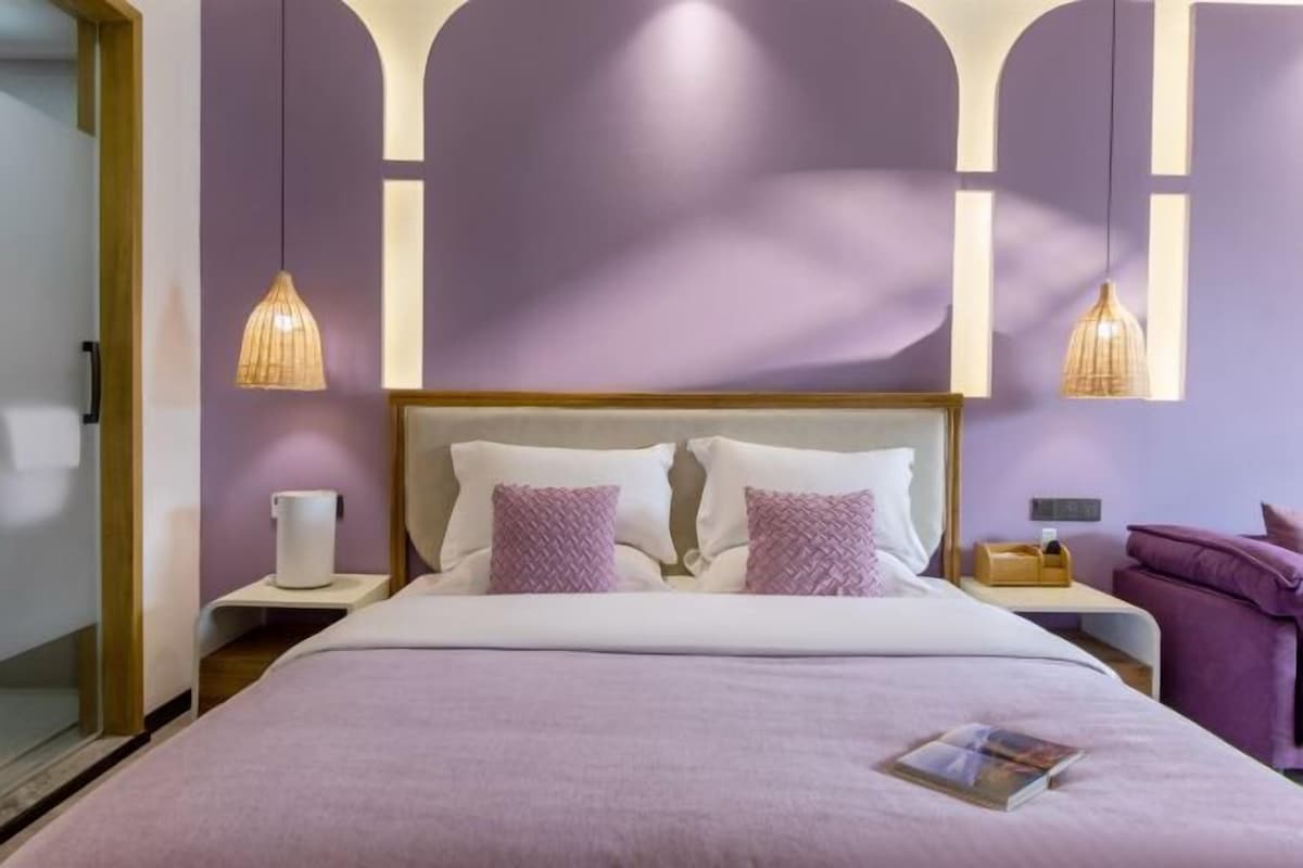 A hotel room with a bed, two bedside tables, a nightstand, a chair, and pendant lights.