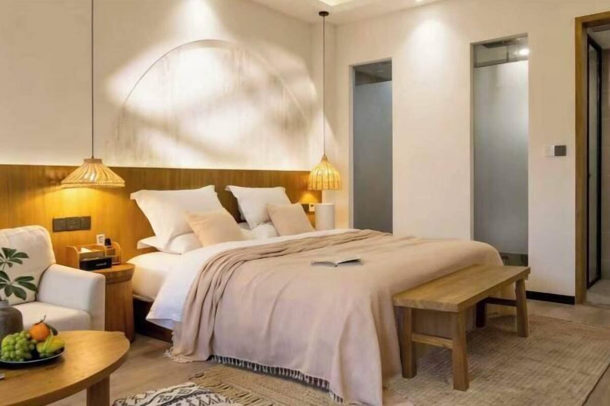 A bedroom with a bed, bedside table, lamp, and a view of a hallway.