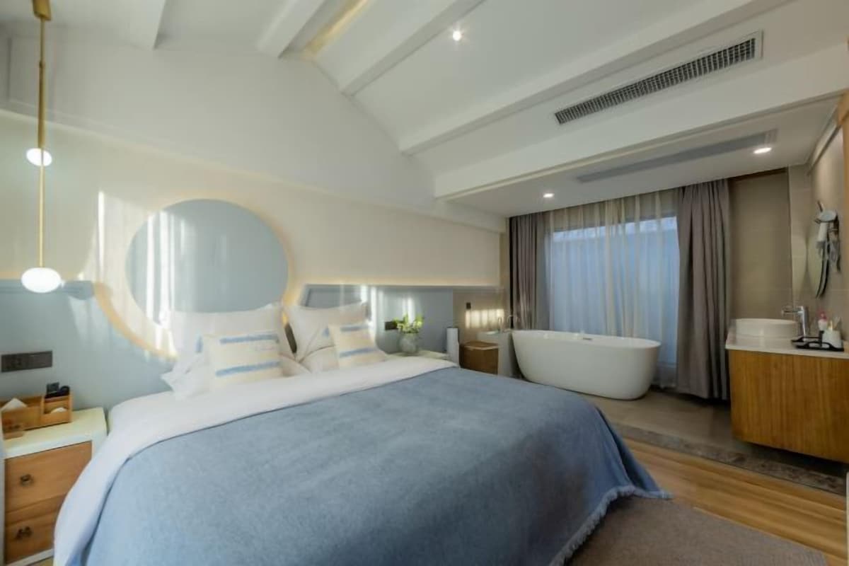 A modern bedroom with a large bed, a bathtub, and a vanity.
