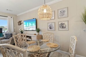 A living room with wicker furniture, a glass table, a flat-screen TV, and framed artwork on the wall. - Driftwood Dreams BEACH condo (Miramar Beach)