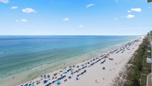 A beach with rows of umbrellas and beach chairs, a pier in the distance, and a clear blue sky. - Direct Beachfront, Wrap Balcony, Breathtaking Views! Shores of Panama (Panama City Beach)