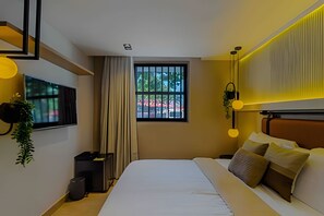 Una camera d'albergo moderna con un letto, una TV, una finestra con tende e una pianta.