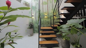A modern staircase with wooden steps and metal railings, surrounded by potted plants and a tropical mural. - Serrezuela Rooms (Cartagena)