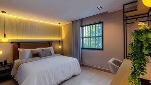 A modern hotel room with a large bed, a desk, and a window with a view of trees. - Serrezuela Rooms (Cartagena)