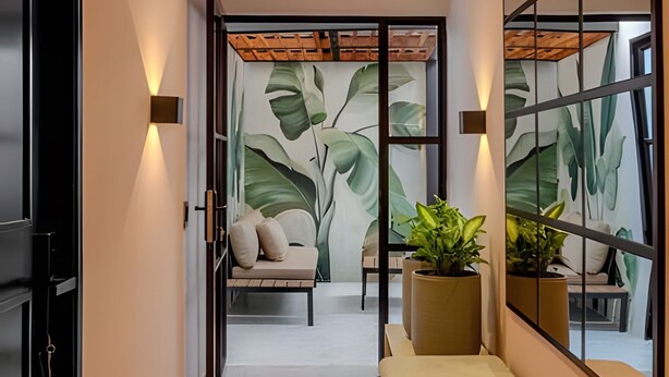 A hallway with a modern interior design, featuring a sofa with cushions, a bench, and a large potted plant. - Serrezuela Rooms (Cartagena)