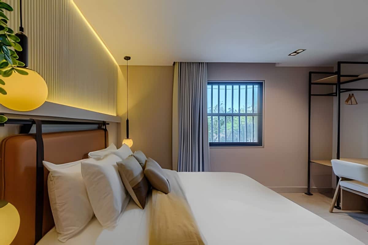 A modern hotel room with a large bed, a desk, and a window with blinds.