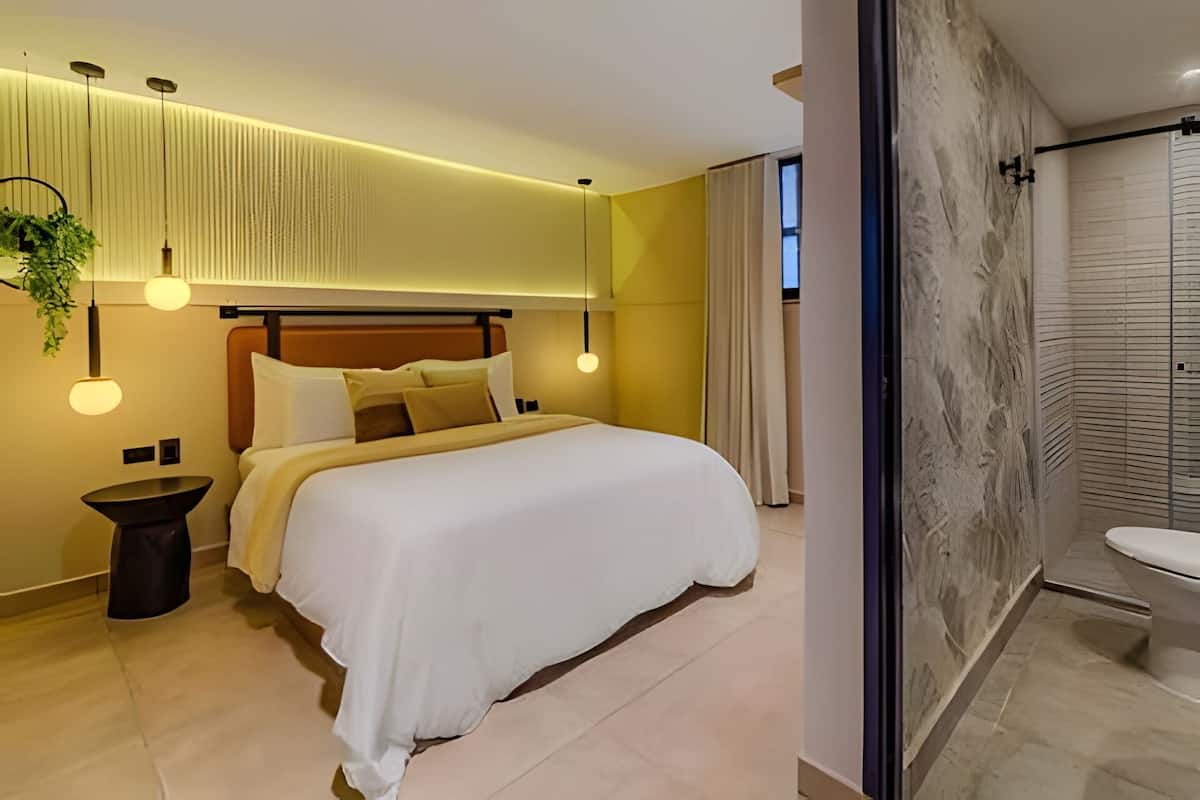 A modern hotel room with a large bed, bedside tables, a hanging plant, and a bathroom with a marble wall and sink.