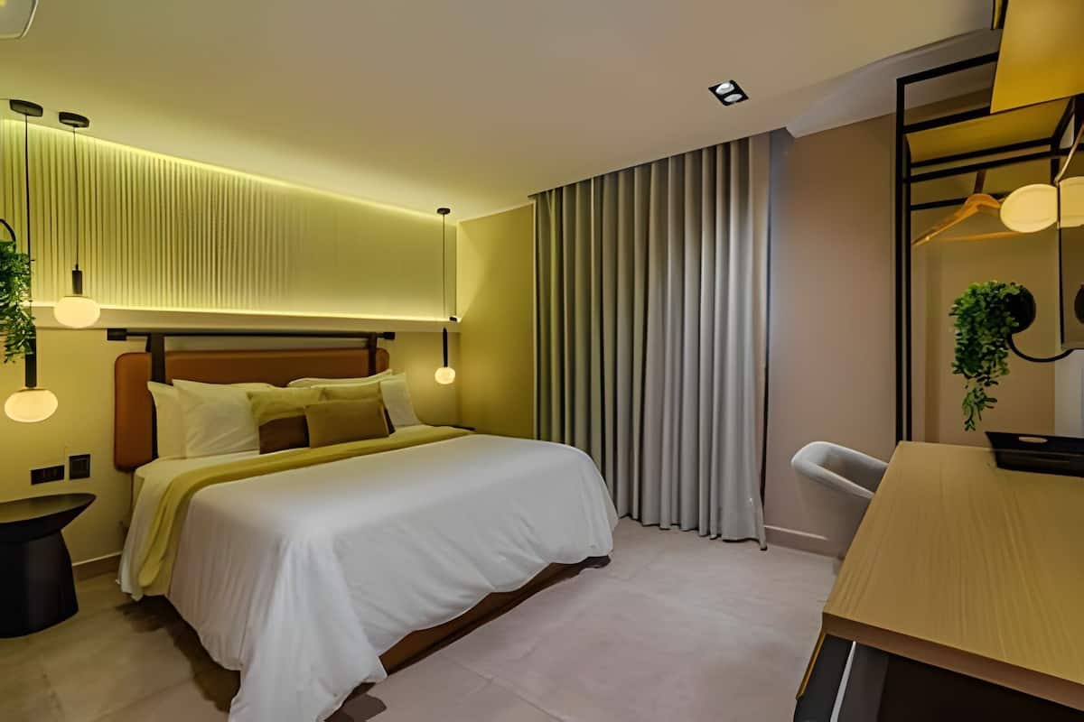A modern hotel room with a large bed, bedside tables, a desk, and a mirror.