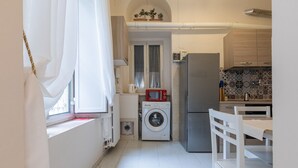 Cocina compacta con lavadora, refrigerador y comedor con una mesa y sillas blancas.