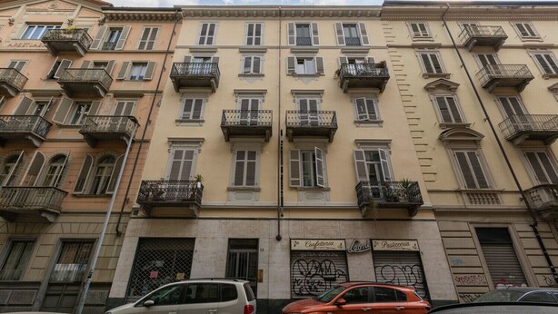 Un edificio de varios pisos con balcones, una entrada a nivel de calle y un cartel que indica una oficina de correos.