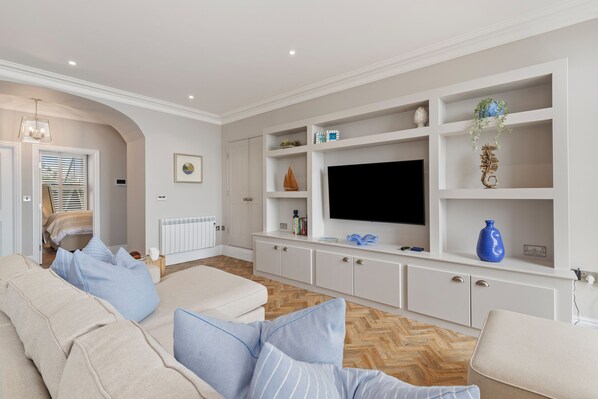 Ein modernes Wohnzimmer mit einem beigefarbenen Sofa, einem Flachbildfernseher und einer weißen Unterhaltungseinheit mit Regalen.