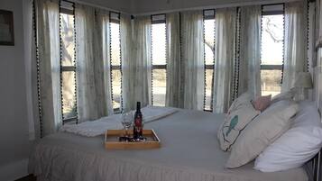 A bedroom with a large bed, a bedside table with a bottle and glass, and curtains with tassels.